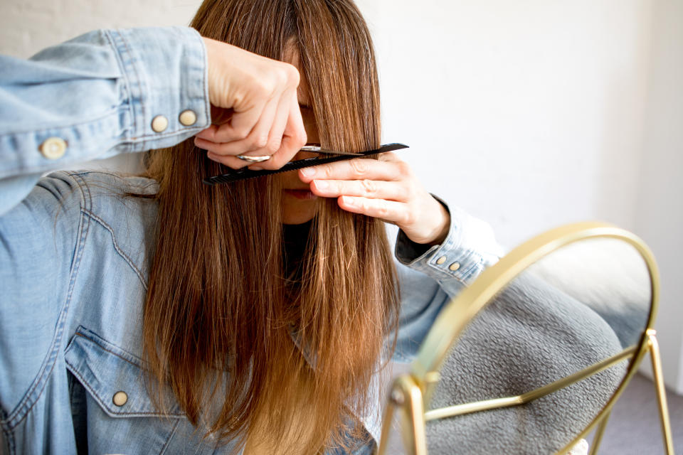 A woman cutting her own hair in front of a mirror