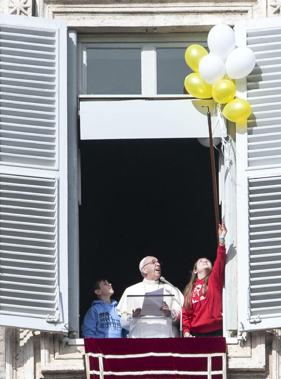 Pope Francis is flanked by two children as they attempt to free colored balloons during the Angelus noon prayer from his window overlooking St. Peter's Square, at the Vatican, Sunday, Feb. 3, 2019. Francis made an urgent appeal for an end to the humanitarian crisis in Yemen on Sunday at the Vatican before boarding a plane to the United Arab Emirates, as he embarked on the first-ever papal trip to the Arabian Peninsula where he is seeking to turn a page in Christian-Muslim relations while also ministering to a unique, thriving island of Catholicism. (Massimo Percossi/ANSA via AP)