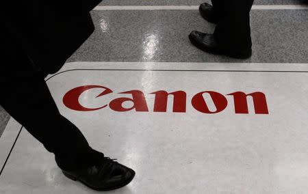 Men walk on an advertisement for Canon Inc at an electronics retail store in Tokyo October 27, 2014. REUTERS/Toru Hanai