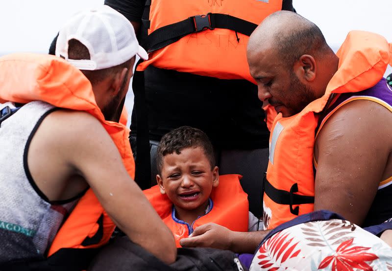 Migrantes esperan en una embarcación de madera a ser rescadatos por la Guardia Costiera italiana en el Mediterráneo