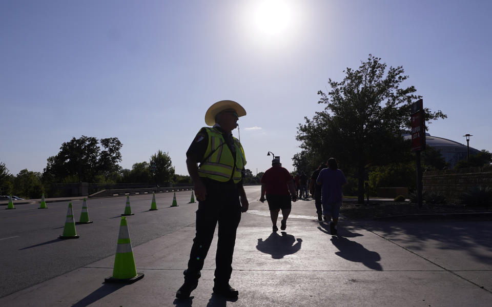 The sun beats down as a police officer stands by to direct pedestrians and traffic after a sporting event in Arlington, Texas, Saturday, Aug. 19, 2023. (AP Photo/LM Otero)