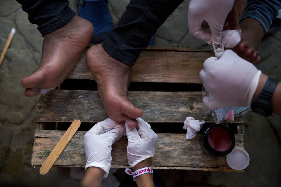 FILE - In this Oct. 26, 2018 file photo, Mexican Red Cross volunteers treat the blistered and cut feet of Central American migrants as their U.S.-bound caravan stops for the night in Arriaga, Mexico. Clamors have grown for buses to transport scores from the caravan to the Mexican capital, where the fatigued travelers hope to find respite and medical treatment, but those buses haven't come. (AP Photo/Rebecca Blackwell, File)