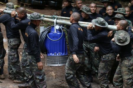 Military personnel carry a water pump machine as they enter the Tham Luang cave complex, where 12 boys and their soccer coach are trapped, in the northern province of Chiang Rai, Thailand, July 6, 2018. REUTERS/Athit Perawongmetha