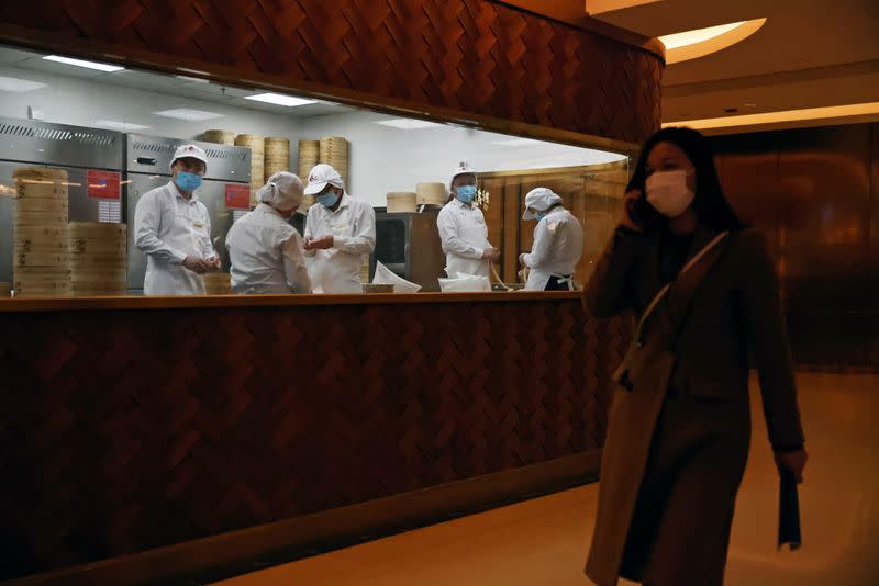 A woman walks past chefs working in a kitchen of a restaurant at a shopping mall in Beijing