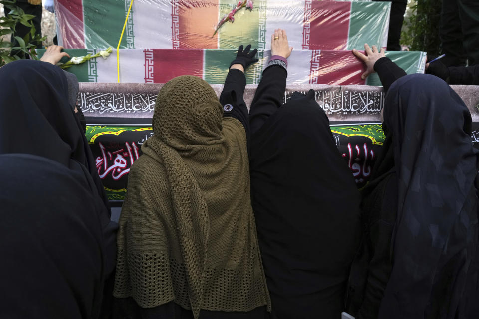 Mourners touch flag-draped coffins of unknown Iranian soldiers who were killed during the 1980-88 Iran-Iraq war, whose remains were recently recovered from former battlefields, during their funeral procession, in Tehran, Iran, Tuesday, Dec. 27, 2022. (AP Photo/Vahid Salemi)