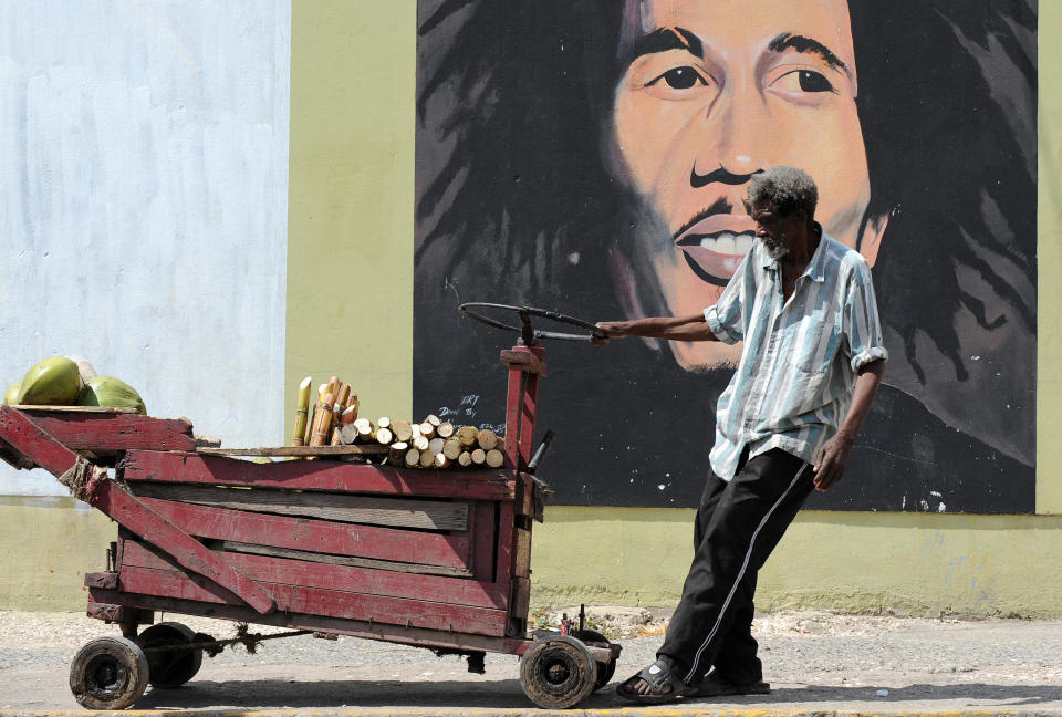 A vendor pulls his cart in front of a mural of late musician Bob Marley in Kingston on February 8, 2009. Marley, who was born in 1945 and died in 1981, remains the most widely known and revered performer of reggae music and is also credited for helping spread Jamaican music to a worldwide audience. Marley's best known hits include "I Shot the Sheriff", "No Woman, No Cry", "Exodus", "Could You Be Loved", "Stir It Up", "Jamming", "Redemption Song", "One Love" and together with The Wailers "Three Little Birds", as well as the posthumous releases "Buffalo Soldier" and "Iron Lion Zion." The compilation album, Legend, released in 1984, three years after his death, is the best-selling reggae album ever with sales of more than 20 million copies.       AFP PHOTO/Jewel SAMAD (Photo credit should read JEWEL SAMAD/AFP via Getty Images)