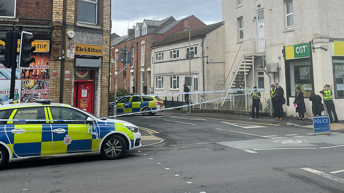 Police cars in front of a cordon, with police officers in the background.