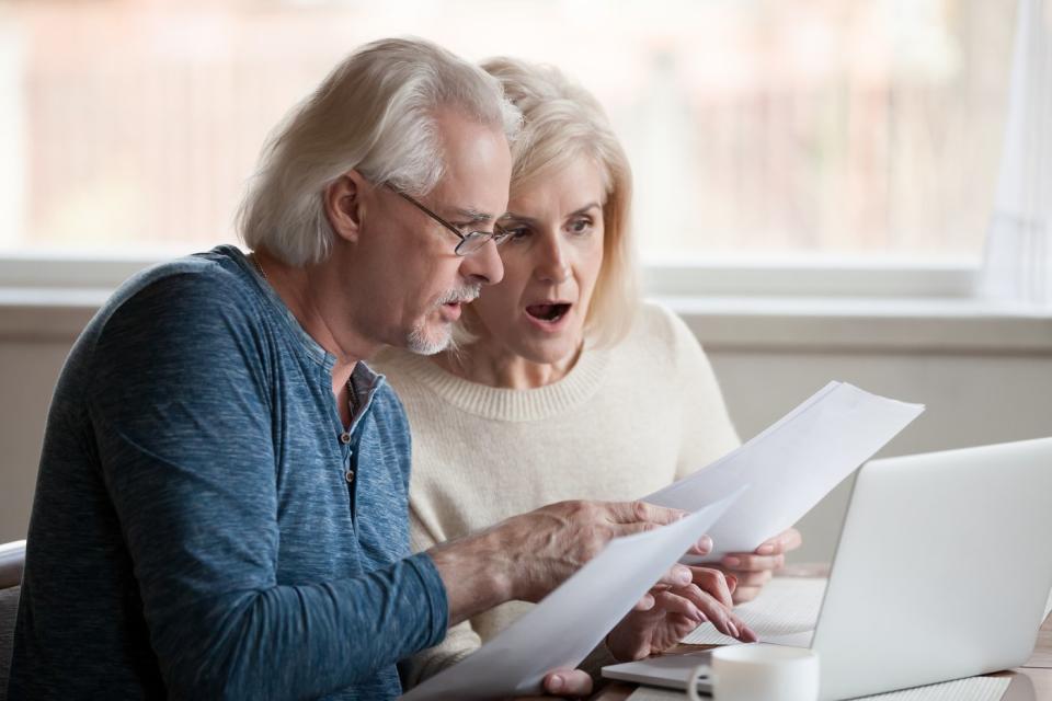 A senior couple looking at a piece of paper with shocked expressions.