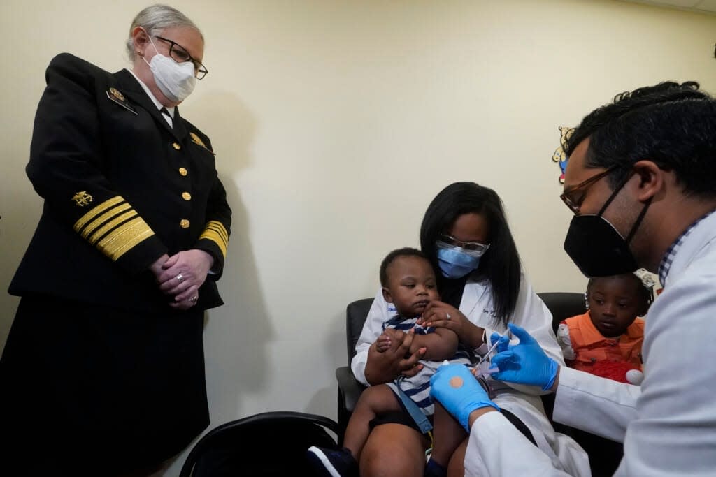 Pediatrician Emy Jean-Marie, center, holds her nine-month-old son, Adedeji Adebayo, on her lap (daughter, Emiola Adebayo, 3, is to her right) as Dr. Nizar Dowla, right, administers a vaccine while Department of Health and Human Services Assistant Secretary for Health, Admiral Rachel Levine, left, observes on Tuesday, June 28, 2022 at the Borinquen Health Care Center in Miami. Florida is the only state that didn’t pre-order the under-5 vaccine, and state Surgeon General Joseph Ladapo has recommended against vaccinating healthy children. (AP Photo/Wilfredo Lee)