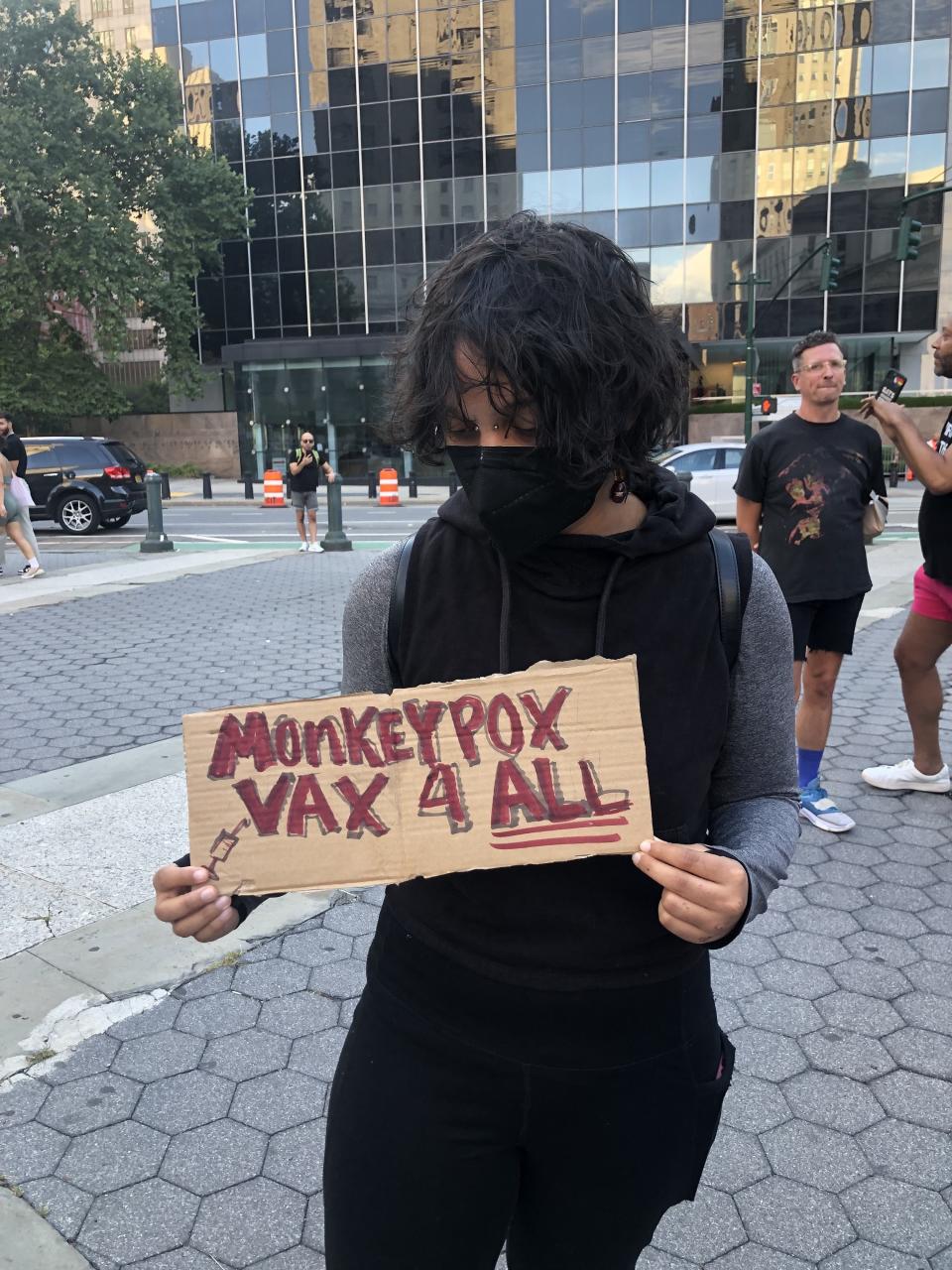 Angel holds their protest sign, "Monkeypox vax 4 all."