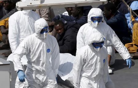 Armed Forces of Malta personnel in protective clothing carry the body of a dead immigrant off the Italian coastguard ship Bruno Gregoretti as surviving migrants watch in Senglea, in Valletta's Grand Harbour April 20, 2015. REUTERS/Darrin Zammit Lupi