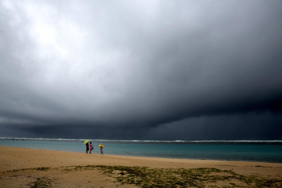 People hold umbrellas as it begins to rain on an otherwise empty beach in Honolulu on Monday, Dec. 6, 2021. A strong storm packing high winds and extremely heavy rain flooded roads and downed power lines and tree branches across Hawaii, with officials warning Monday of potentially worse conditions ahead. 