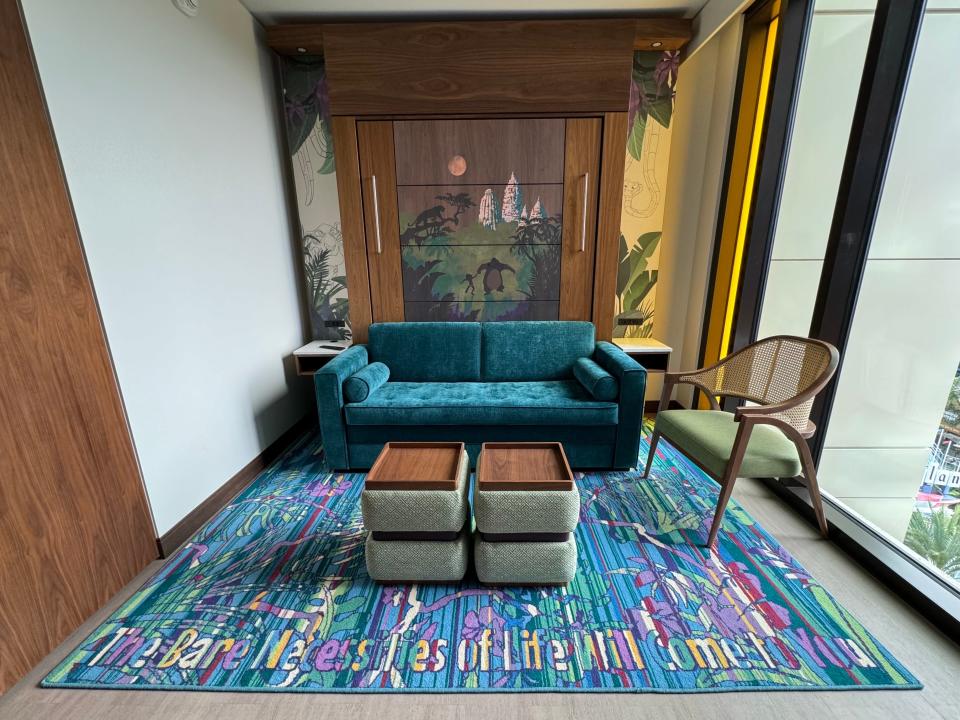 Small blue couch in front of pull-down bed wall with Jungle Book mural on top of colorful carpet in Disneyland duo studio