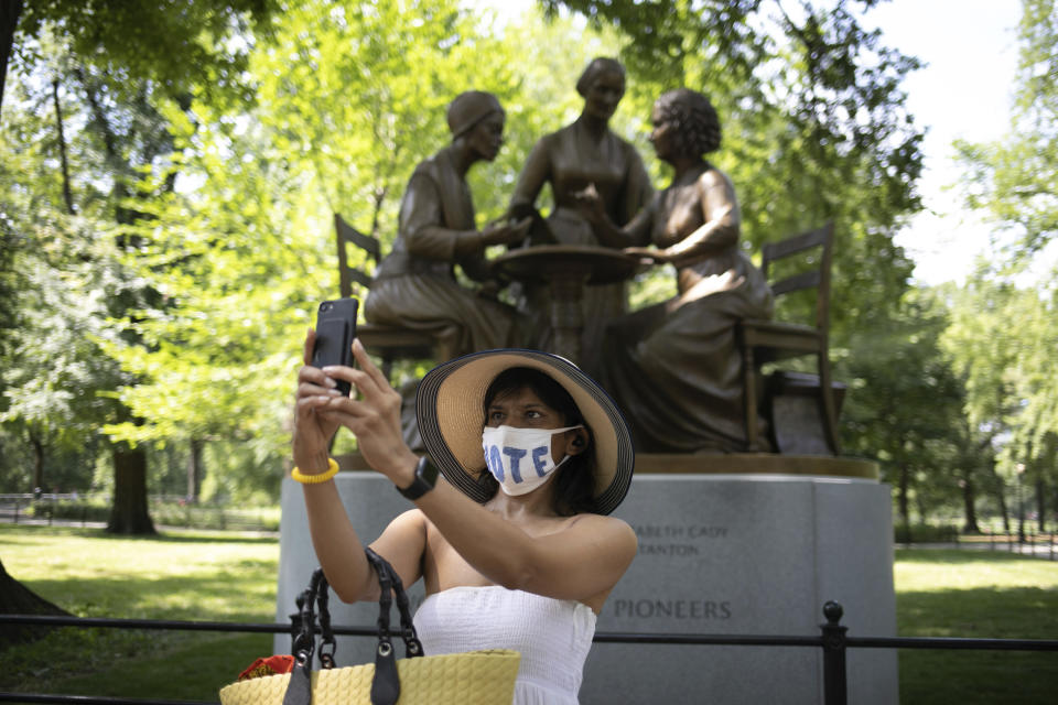 Reshma Patel takes a photo in front of Women's Rights Pioneers statue in Central Park Wednesday, Aug. 26, 2020, in New York. The statue, created by sculptor Meredith Bergmann and featuring Sojourner Truth, Susan B. Anthony and Elizabeth Cady Stanton, is the first monument in the park honoring any female historical figures. (AP Photo/Kevin Hagen)