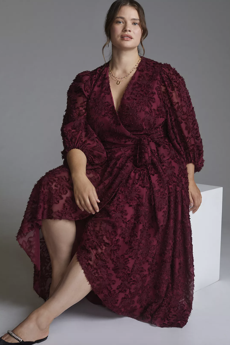 plus size white model with brown hair sitting in burgundy red wrap dress