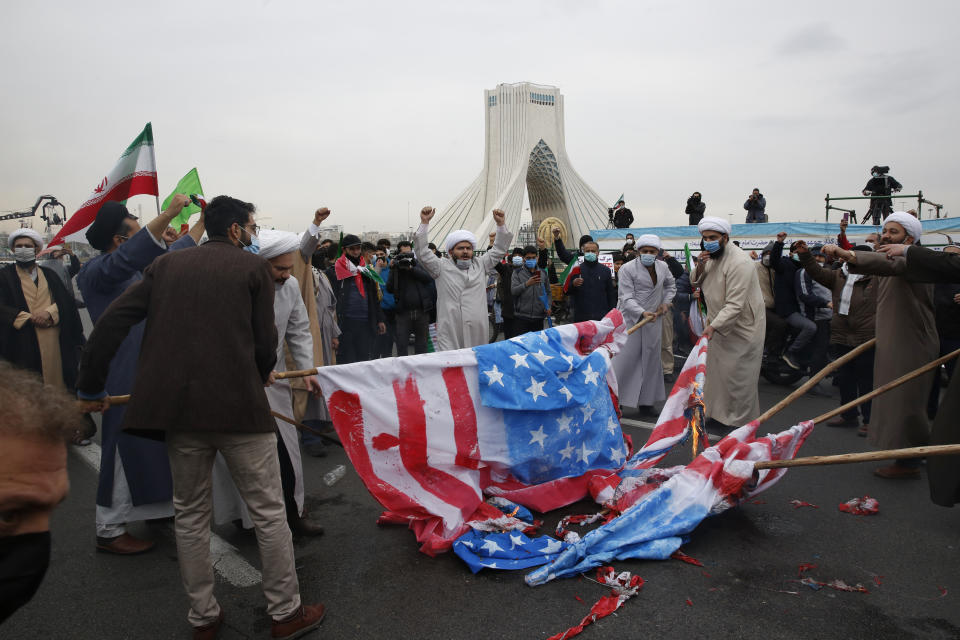 Clerics burn representations of the U.S. flag during the annual rally commemorating the anniversary of Iran's 1979 Islamic Revolution in Azadi (freedom) Square in Tehran, Iran, Friday, Feb. 11, 2022. Thousands of cars and motorbikes paraded in the celebration, although fewer pedestrians were out for a second straight year due to concerns over the coronavirus pandemic. (AP Photo/Vahid Salemi)