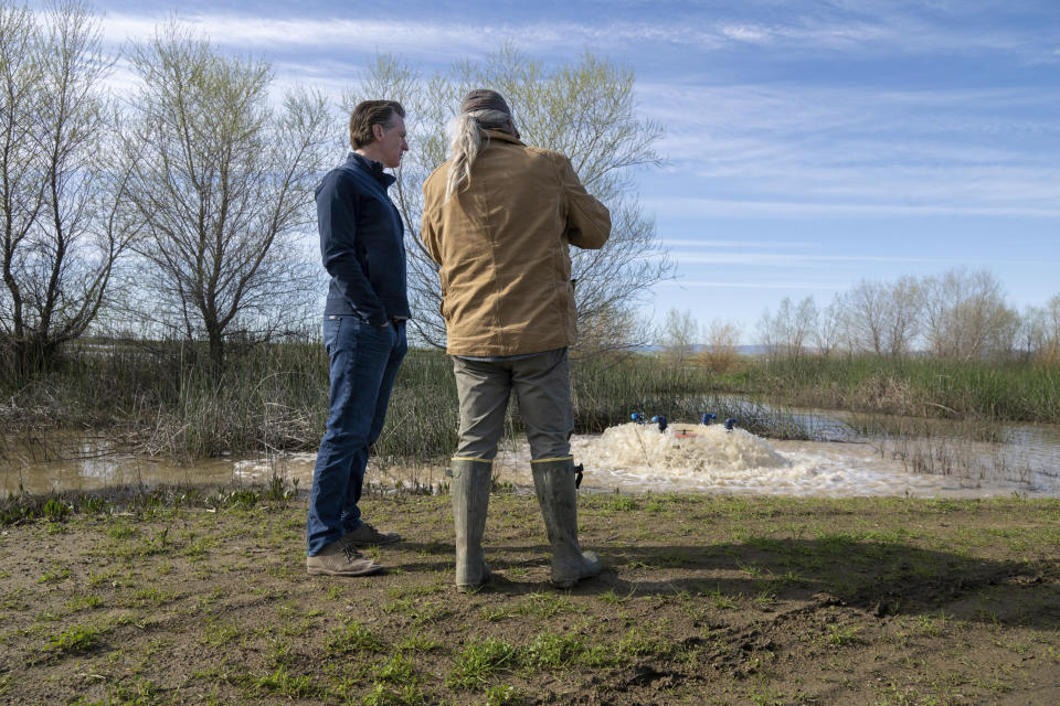 California Gov. Gavin Newsom, left, observes how recycled collected water floods a property at the 810 acres of farmland owned by Brian and Elena Corral to recharge Yolo County's groundwater aquifer in Dunnigan, Calif., on Friday, March 24, 2023. California Gov. Gavin Newsom ended some of the state's water restrictions on Friday because a winter of relentless rain and snow has replenished the state's reservoirs and eased fears of a shortage after three years of severe drought. (Paul Kitagaki Jr./The Sacramento Bee via AP)