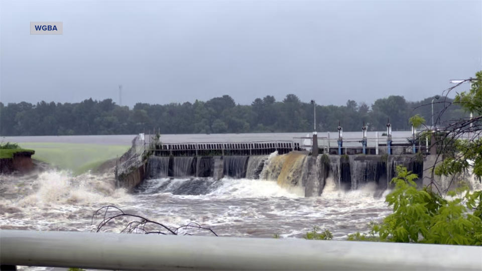 This image taken from video provided by WGBA-TV, shows water breaching a section of a dam, left, along the Little Wolf River, Friday, July 5, 2024, in Manawa, Wis. (WGBA-TV via AP)