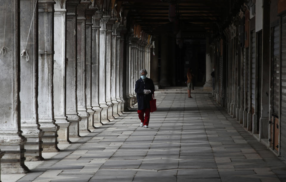 In this picture taken on Wednesday, May 13, 2020, a woman wearing a sanitary mask walks at St. Mark's Square in Venice, Italy. Venetians are rethinking their city in the quiet brought by the coronavirus pandemic. For years, the unbridled success of Venice's tourism industry threatened to ruin the things that made it an attractive destination to begin with. Now the pandemic has ground to a halt Italy’s most-visited city, stopped the flow of 3 billion euros in annual tourism-related revenue and devastated the city's economy. (AP Photo/Antonio Calanni)