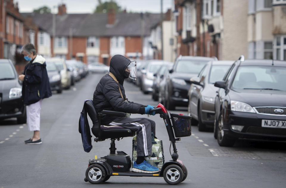 A man wearing a protective visor crosses the road on a mobility scooter, England, Monday June 29, 2020. The British government is reimposing lockdown restrictions in the central England city of Leicester after a spike in coronavirus infections, including the closure of shops that don’t sell essential goods and schools. (Joe Giddens/PA via AP)