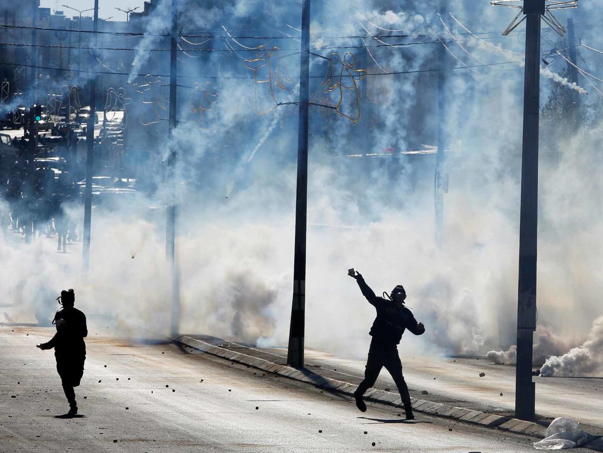 A Palestinian protester yesterday hurls stones as tear gas is fired by Israeli troops: Reuters