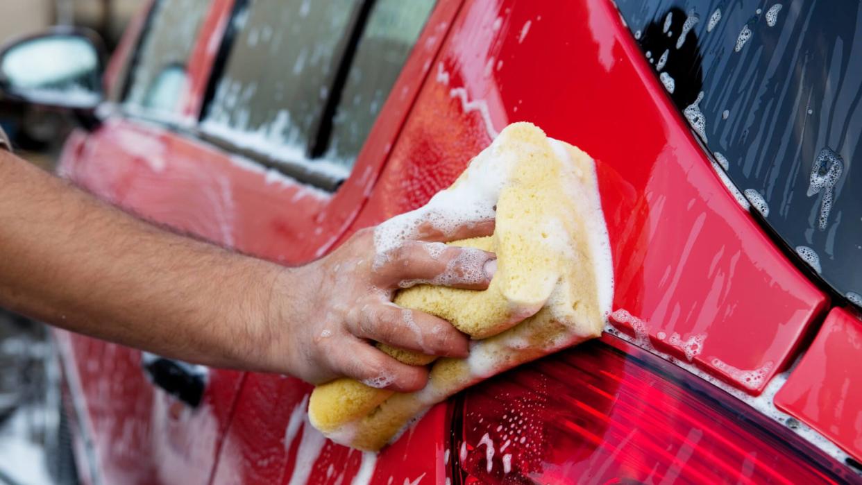 washing a red car with yellow sponge.