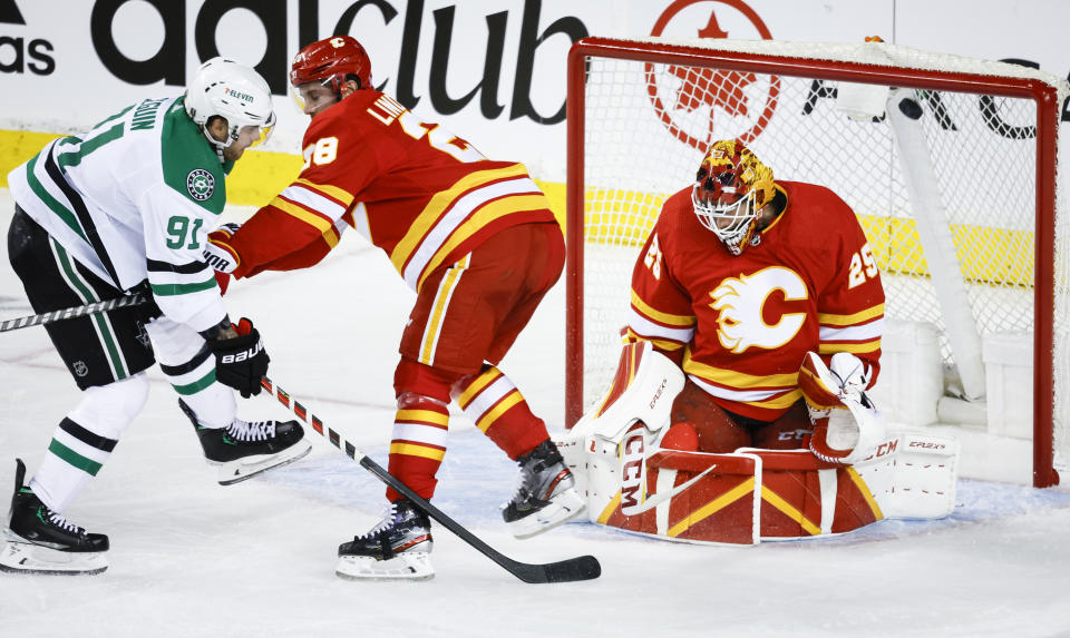 Dallas Stars center Tyler Seguin, left, shoots wide of Calgary Flames goalie Jacob Markstrom, right, as Flames center Elias Lindholm defends during the first period of Game 1 of an NHL hockey first-round playoff series Tuesday, May 3, 2022, in Calgary, Alberta. (Jeff McIntosh/The Canadian Press via AP)