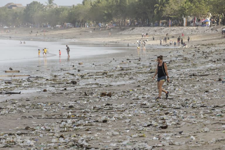 BALI, INDONESIA - DECEMBER 29: Tourists walk among plastic trash and discarded wood on the shore of Kuta Beach in Bali, Indonesia on December 29, 2022. During monsoon, Bali's popular Kuta Beach is affected by tons of marine pollution. Trashes of plastic rubbish, woods and other discarded materials washed ashore along the coastline. (Photo by Johannes P. Christo/Anadolu Agency via Getty Images)