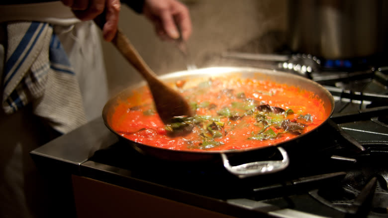 person stirring tomato sauce