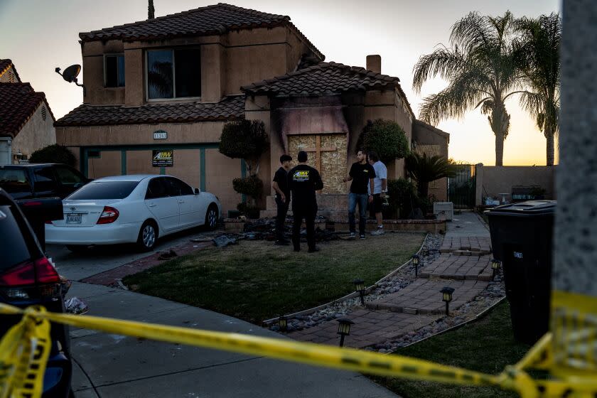 RIVERSIDE, CA - NOVEMBER 29, 2022: Workers from AHW, a fire damage company, install a wooden cross to a boarded up window at the home where three family members were murdered Friday in the 111200 block of Price Court on November 29, 2022 in Riverside, California. The murders and burning home are thought to be connected to the attempted abduction of a teenage girl. The girl is safe.(Gina Ferazzi / Los Angeles Times)