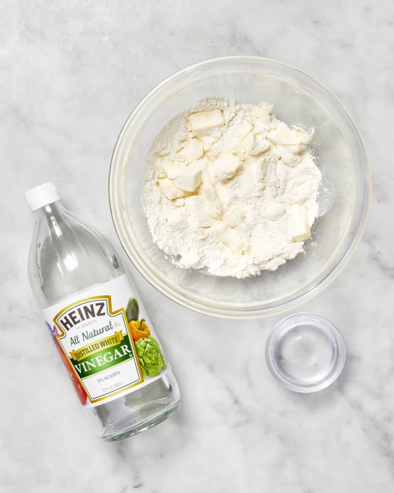 A bowl with flour and cubes of butter and a bottle of vinegar to make a pie crust seen from above.