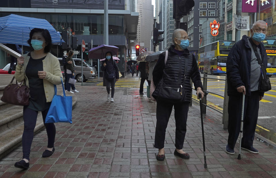 People wearing protective face masks walk on a street in the rain in Hong Kong, Friday, Feb. 14, 2020. COVID-19 viral illness has sickened tens of thousands of people in China since December. (AP Photo/Vincent Yu)