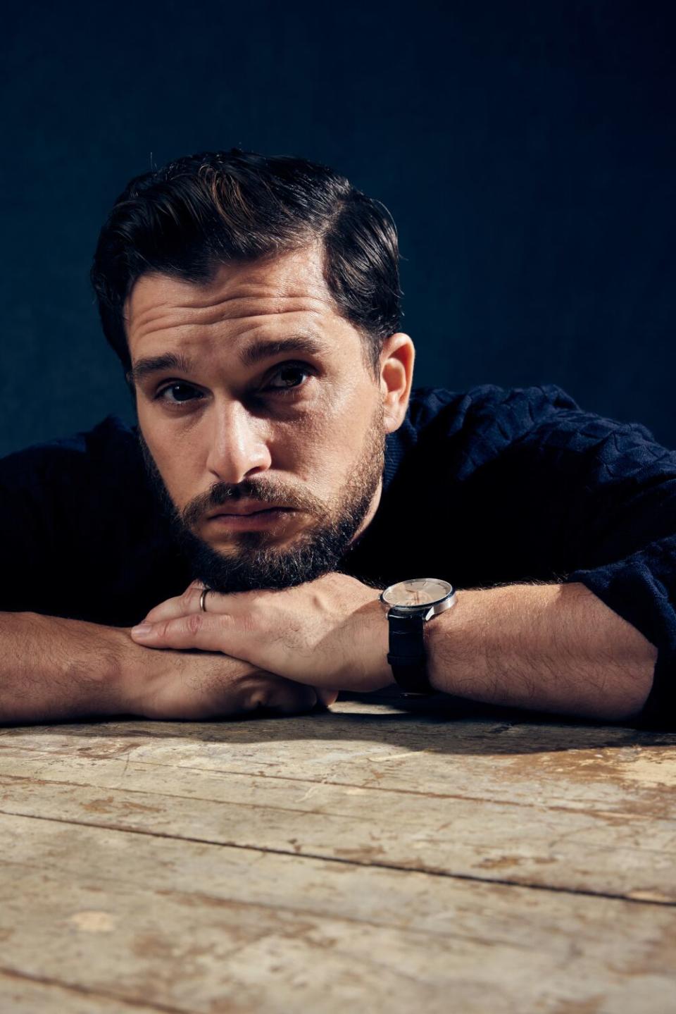 An actor rests his chin on his hands on a table