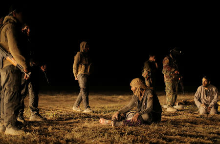 Fighters from the Syrian Democratic Forces (SDF) stand near evacuated civilians, near the village of Baghouz, Deir Al Zor province, in Syria March 9, 2019. REUTERS/Rodi Said