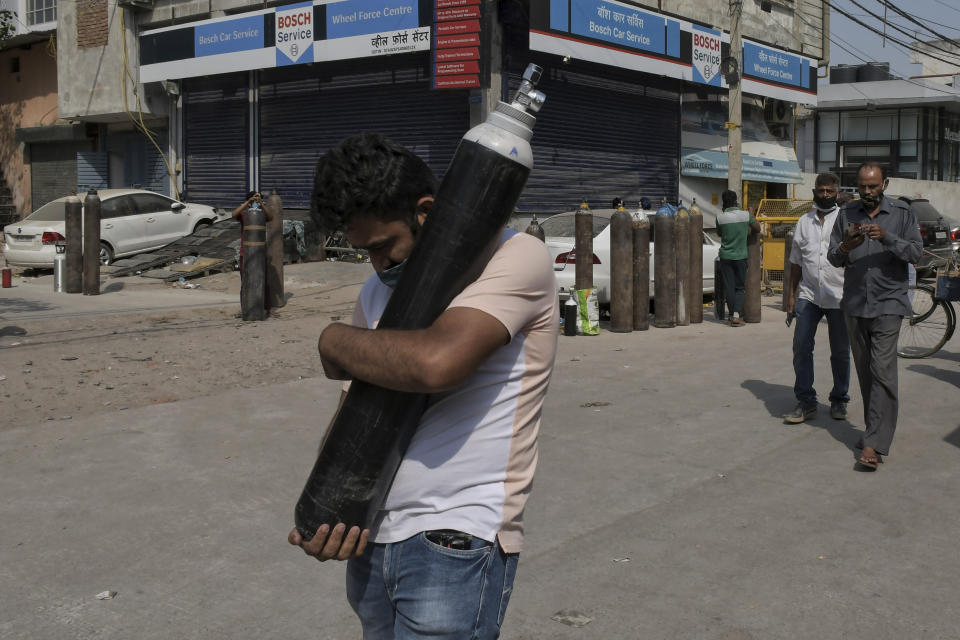 A man walks carrying a refilled cylinder as family members of Covid-19 patients wait in queue to refill their oxygen cylinders at Mayapuri area in New Delhi, India.