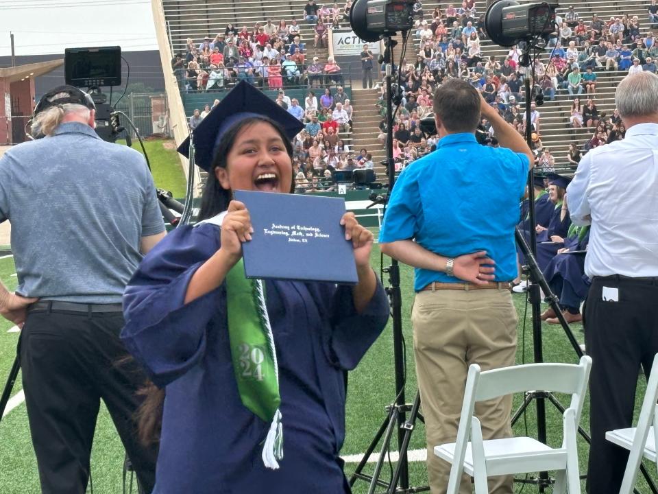 An ATEMS High School graduate shows off her diploma to her family in the stands at Shotwell Stadium on Saturday