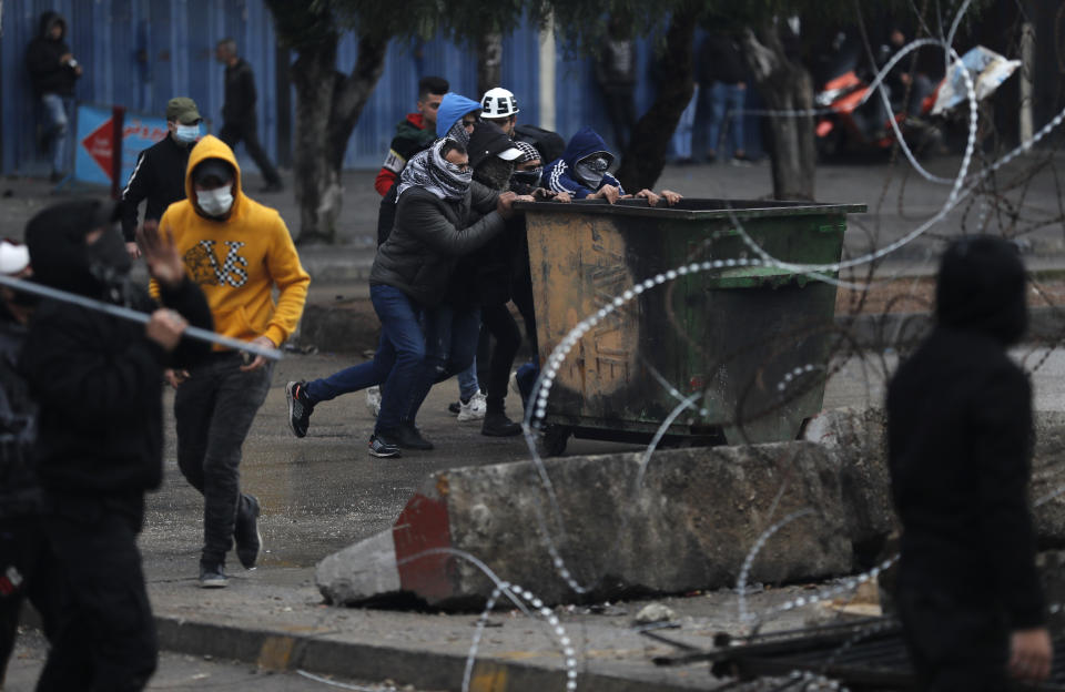 Protesters move a garbage container in an attempt to break the main door of an official government office during a protest against deteriorating living conditions and strict coronavirus lockdown measures, in Tripoli, north Lebanon, Thursday, Jan. 28, 2021. Violent confrontations between protesters and security forces over the last three days in northern Lebanon left a 30-year-old man dead and more than 220 people injured, the state news agency said Thursday. (AP Photo/Hussein Malla)