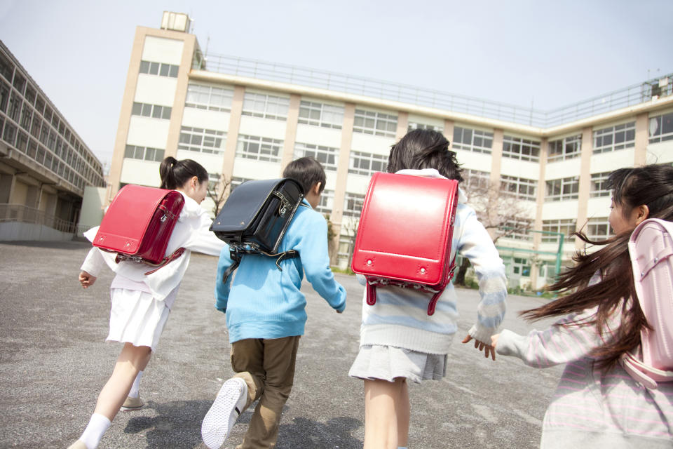 Four students with backpacks running joyfully in a schoolyard