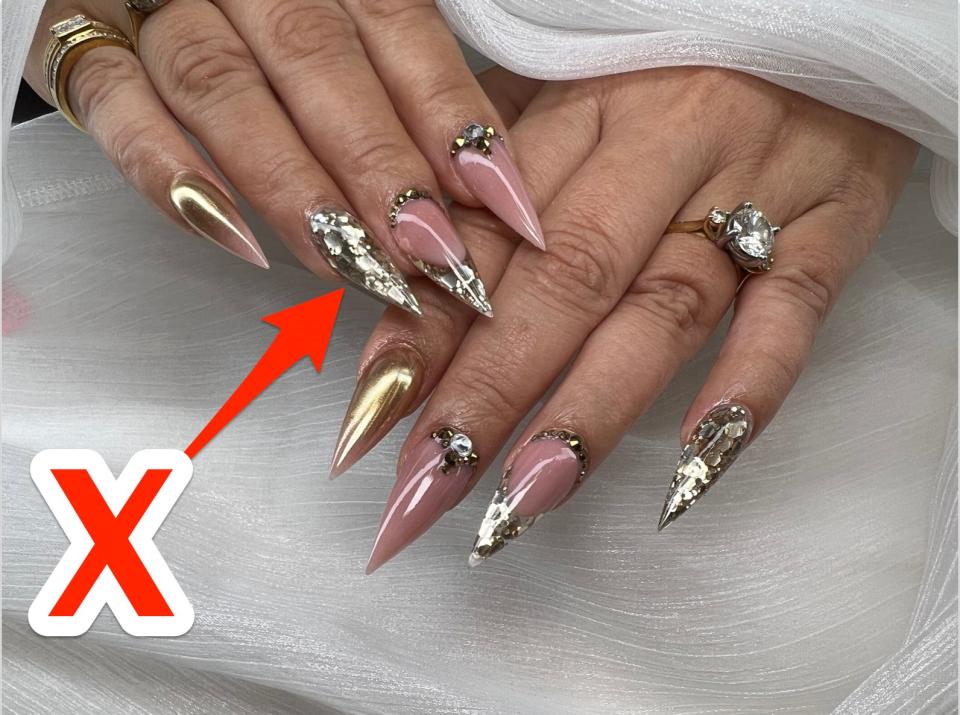 An X pointing at a super blinged-out nail.