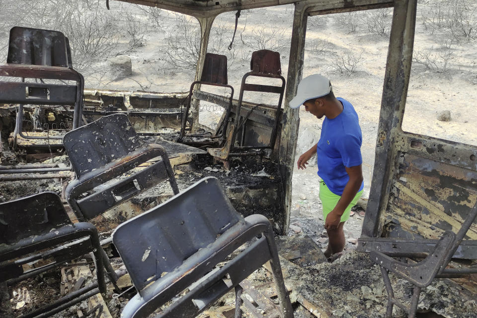 A man watches a charred van in a village of the region of El Tarf, near the northern Algerian-Tunisian border, Thursday, Aug.18, 2022. Wildfires raging in the forests of eastern Algeria have killed at least 26 people, according to a "provisional report" by the north African country's interior minister. (AP Photo/Mohamed Ali)