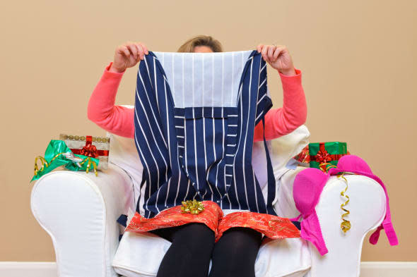 A woman opening Christmas presents to discover she got an apron and some underwear.