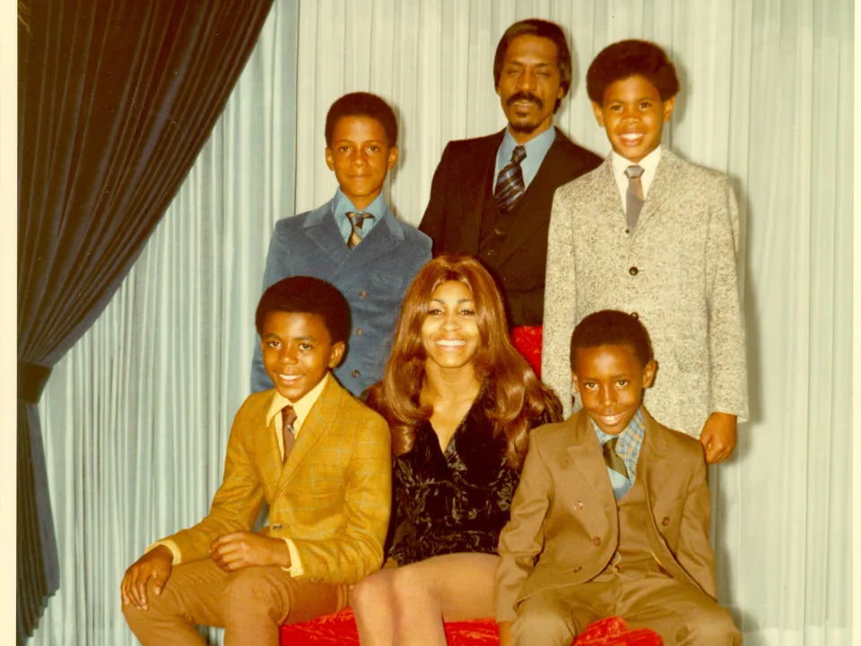 A family photo of the Turners and their sons sitting on a red ottoman.