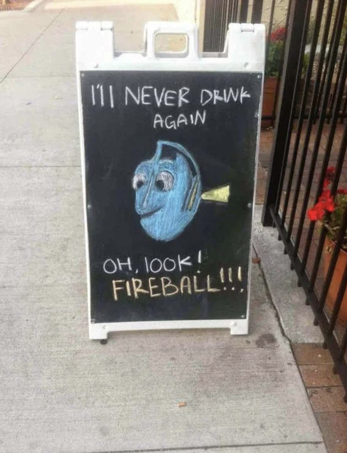 Chalkboard sign on a sidewalk shows a drawing of Dory from Finding Nemo with text: "I'll never drink again. Oh, look! Fireball!!!"