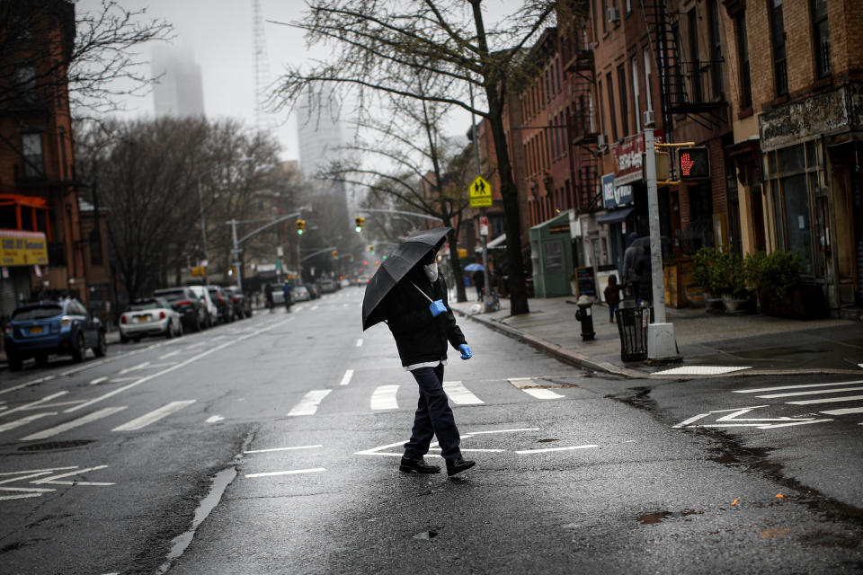 A pedestrian wearing a protective mask and protective gloves walks across an empty Dekalb Avenue, Sunday, March 29, 2020, in Brooklyn borough of New York. The new coronavirus causes mild or moderate symptoms for most people, but for some, especially older adults and people with existing health problems, it can cause more severe illness or death. (AP Photo/John Minchillo)