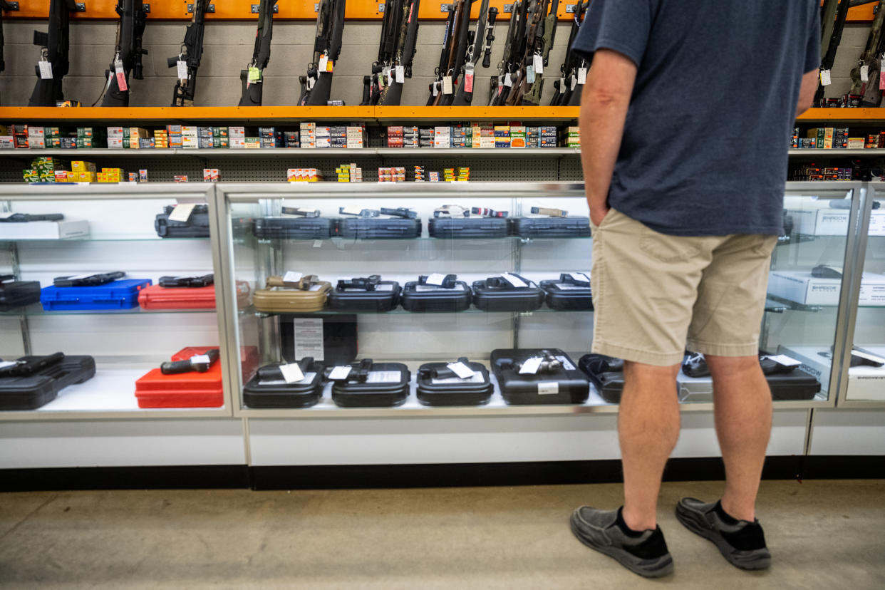 Seen looking over a counter of handguns at an array of rifles, a customer ponders a purchase.