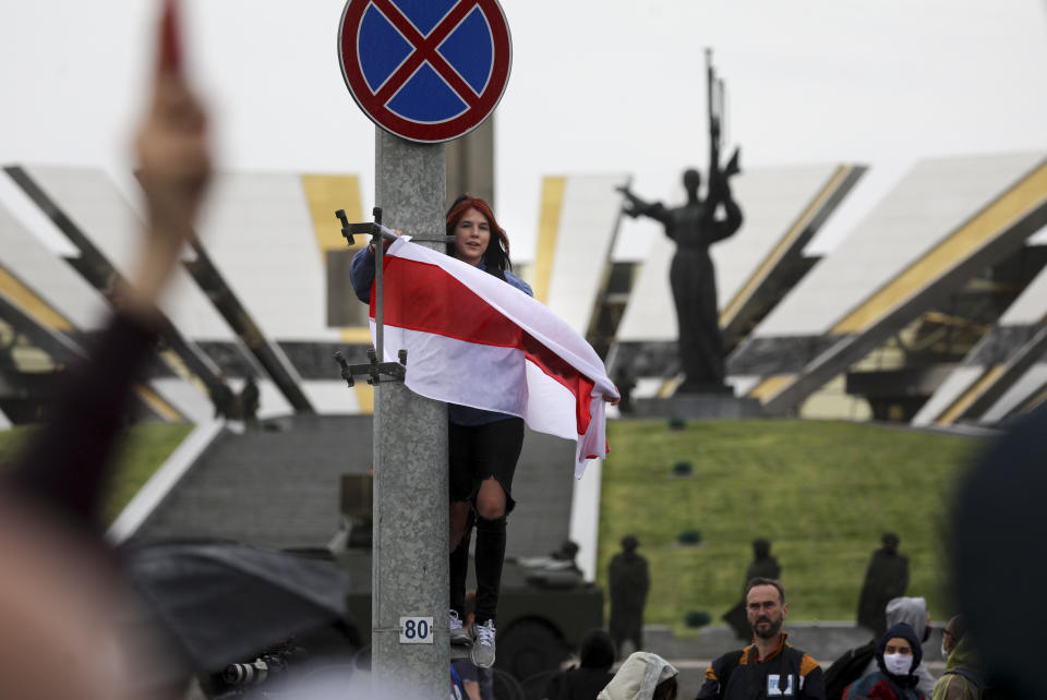 A woman holds an old Belarusian national flag at the WWII monument during an opposition rally to protest the official presidential election results in Minsk, Belarus, Sunday, Sept. 27, 2020. Tens of thousands of demonstrators marched in the Belarusian capital calling for the authoritarian president's ouster, some wearing cardboard crowns to ridicule him, on Sunday as the protests that have rocked the country marked their 50th consecutive day. (AP Photo/TUT.by)