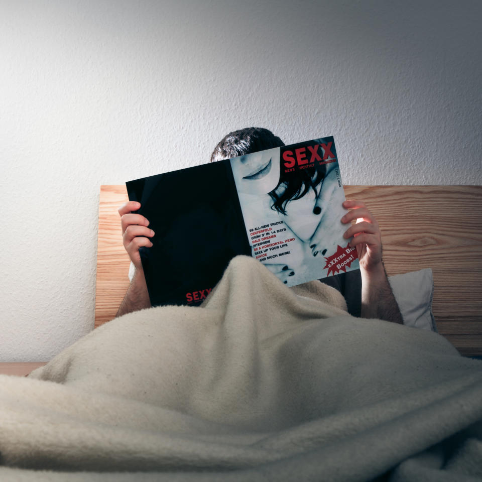 A man in bed reading a porn magazine