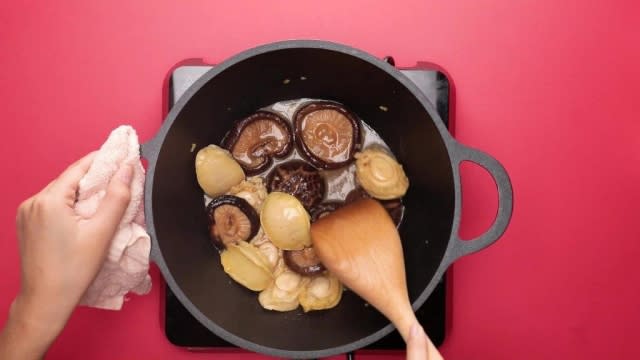 Stirring mushrooms and abalones in a pot with wooden spatula