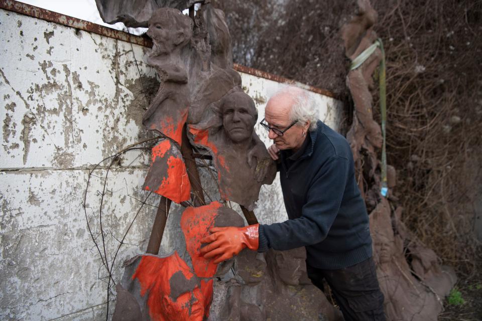 A man leans over a Pillar of Shame sculpture as he applies applies paint.