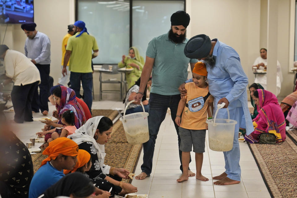 Raghuvinder Singh, right, greets a child while helping to serve food after a Sikh worship service at a gurdwara in Glen Rock, N.J., Sunday, Aug. 15, 2021. Baba Punjab Singh, a Sikh priest visiting from India, was shot in the head by a white supremacist Army veteran in Wisconsin in 2012, and left partially paralyzed. He died from his wounds in 2020. Over seven years, the priest’s son, Raghuvinder Singh, split his time between caring for his father in Oak Creek and working in Glen Rock, New Jersey, as assistant priest at a gurdwara there. Raghuvinder said the greatest lesson his father taught him was how to embody “chardi kala,” which calls for steadfast optimism in the face of oppression. (AP Photo/Seth Wenig)